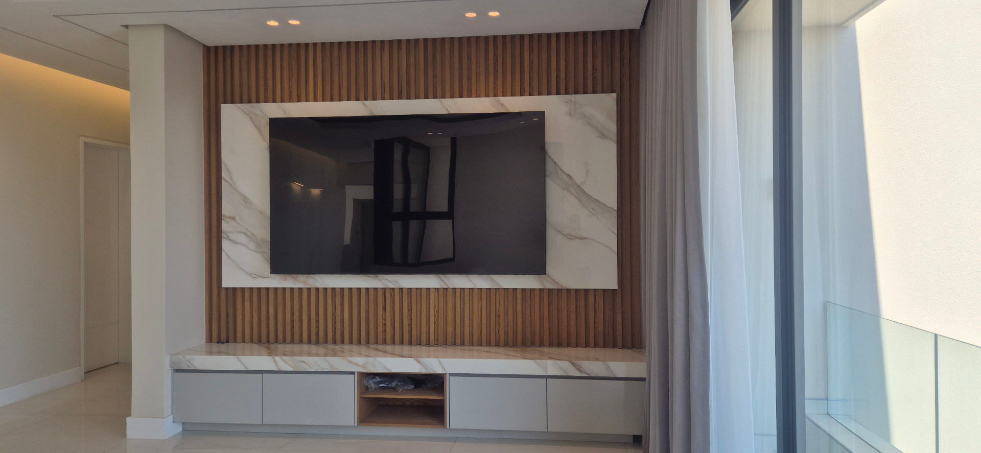 Large TV mounted on marble slab and oak slat wall in a lounge